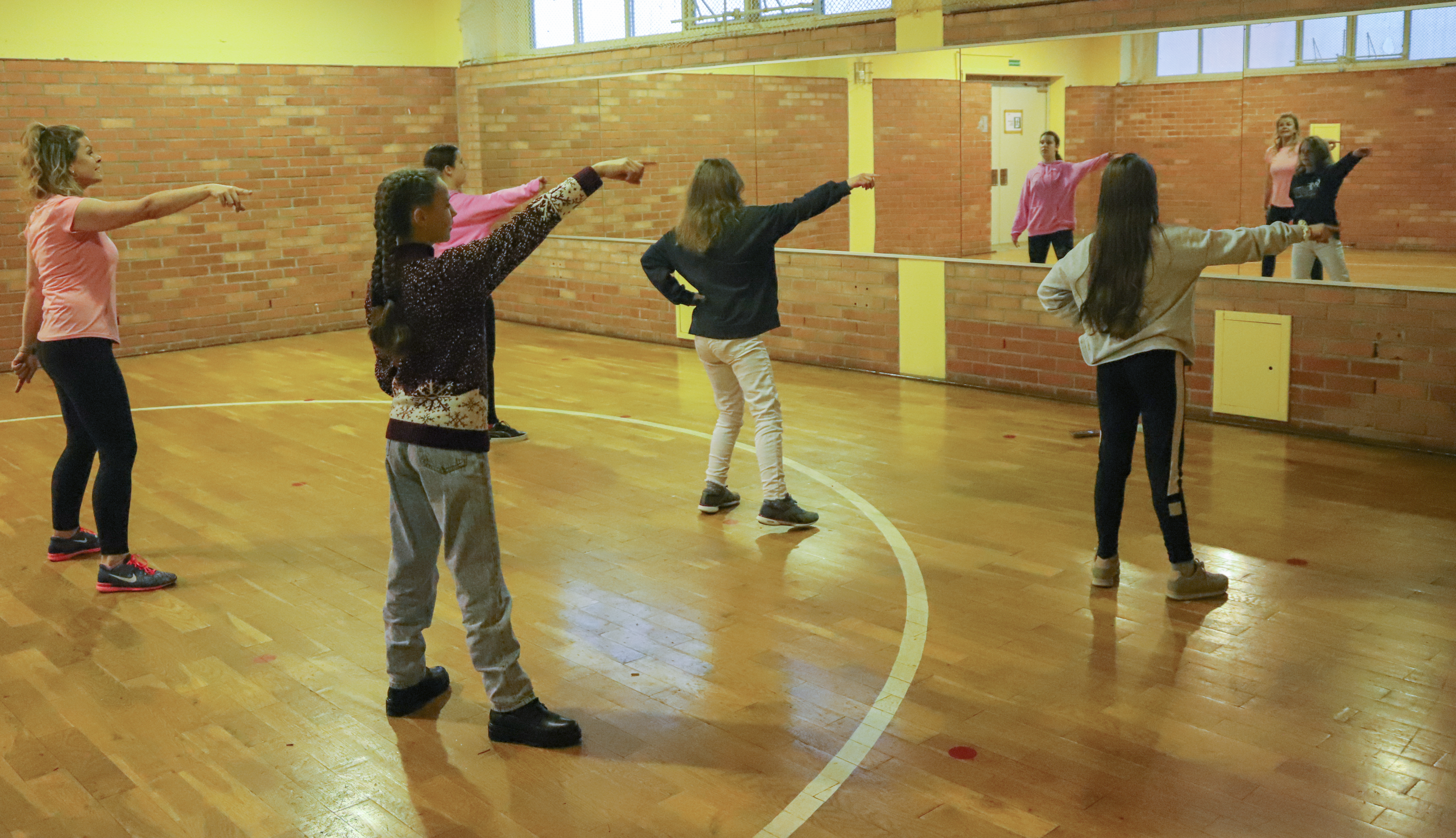 Jugendliche tanzen synchron in einer Sporthalle vor einem großen Spiegel.