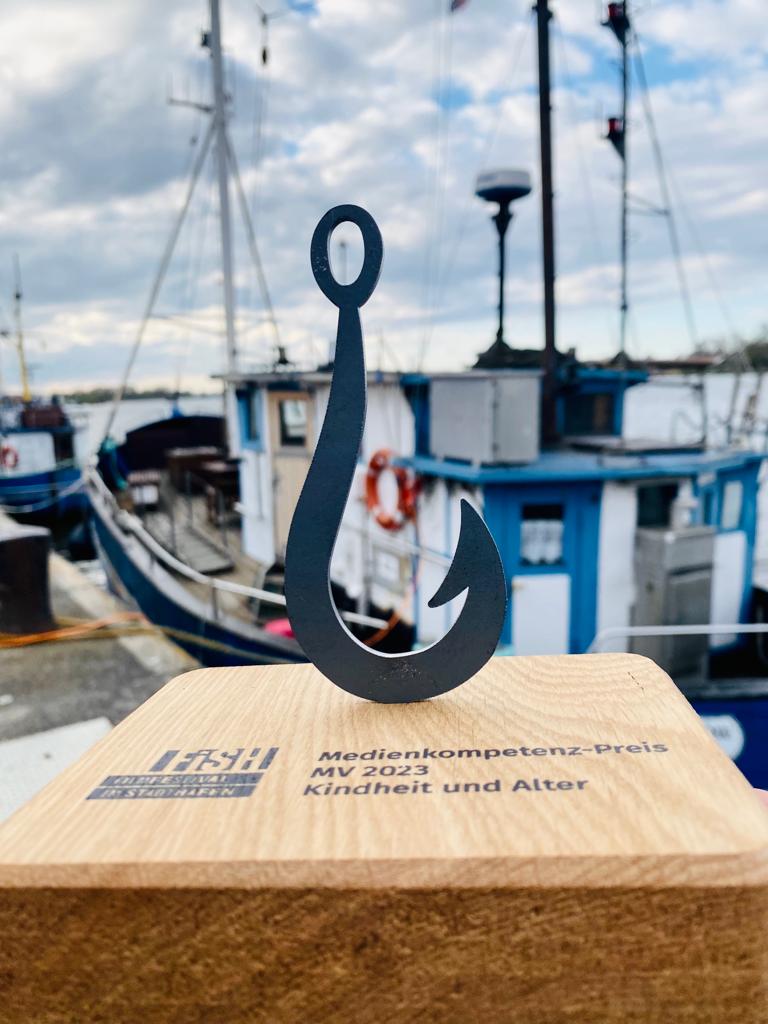 Trophäe des Medienkompetenz-Preises M-V vor dem Hintergrund eines Bootes am Rostocker Hafen.