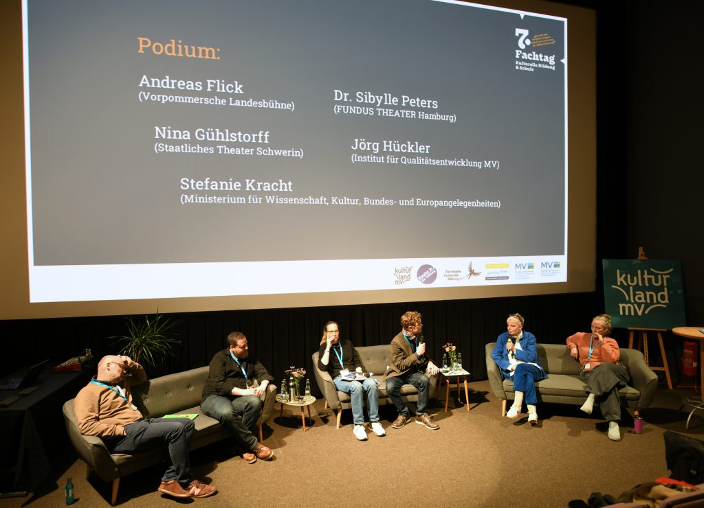 fünf Menschen sitzen zusammen mit dem Moderator auf einer Bühne im Halbkreis
